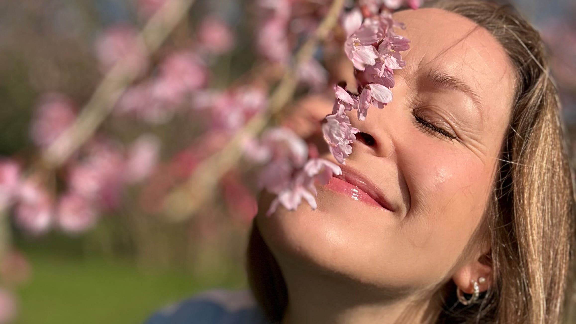 Camilla Dyer, founder of ERA Life First, with eyes closed in spring blossom sunshine — female founder wellbeing and nervous system advocate