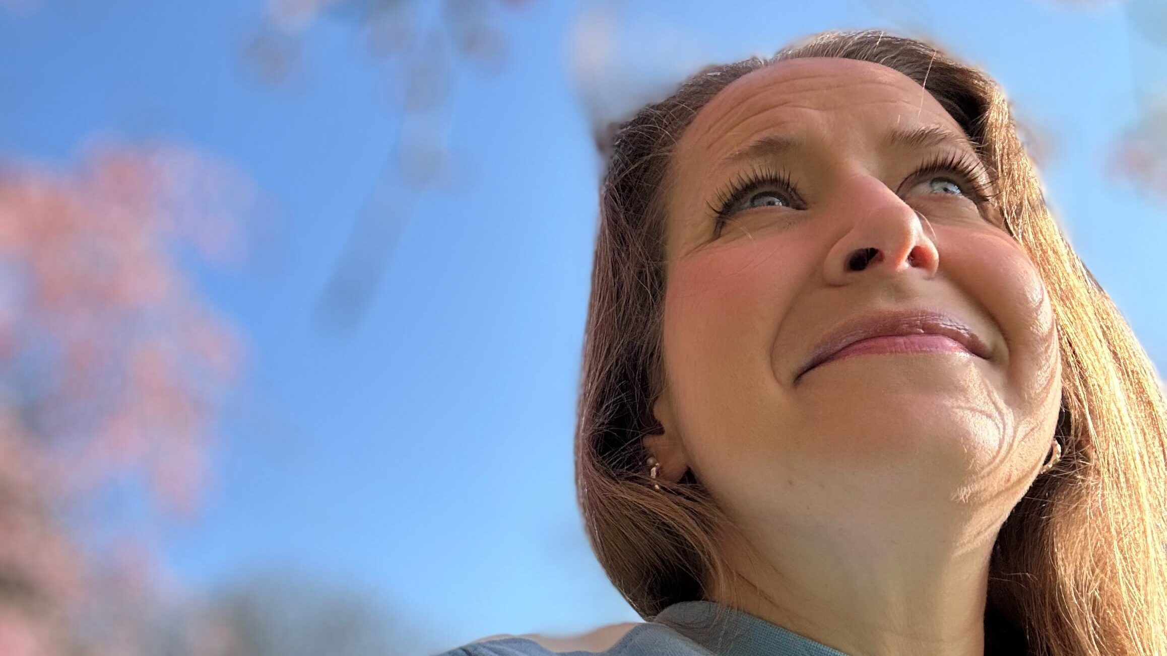 Camilla Dyer — female founder wellbeing advocate — looking up into pink blossom against a blue spring sky, ERA Life First launch day Spring Equinox 2026